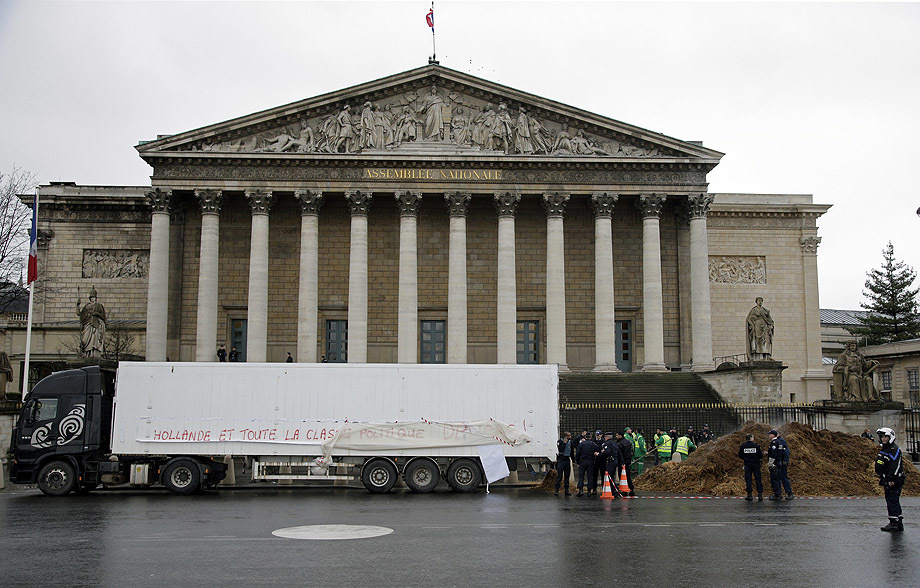 French police stand guard near a lorry that displays a protest banner reading and a large pile of manure in front of the National Assembly in Paris,