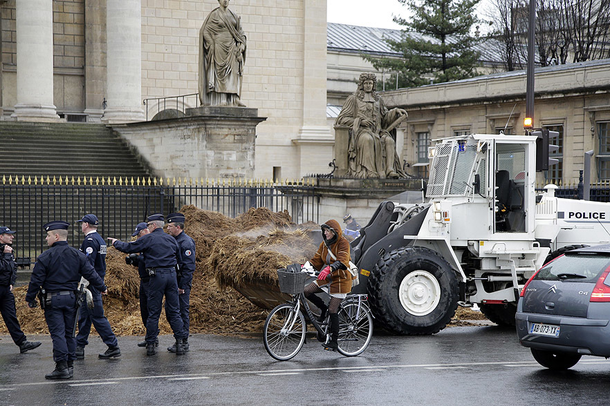 A woman rides a bicycle past French police as a large pile of manure is removed in front of the National Assembly in Paris